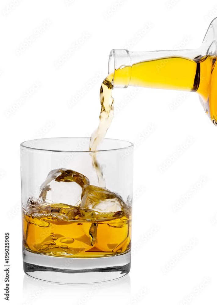 Golden whiskey pours from bottle into glass with ice Golden whiskey pours from bottle into glass with ice