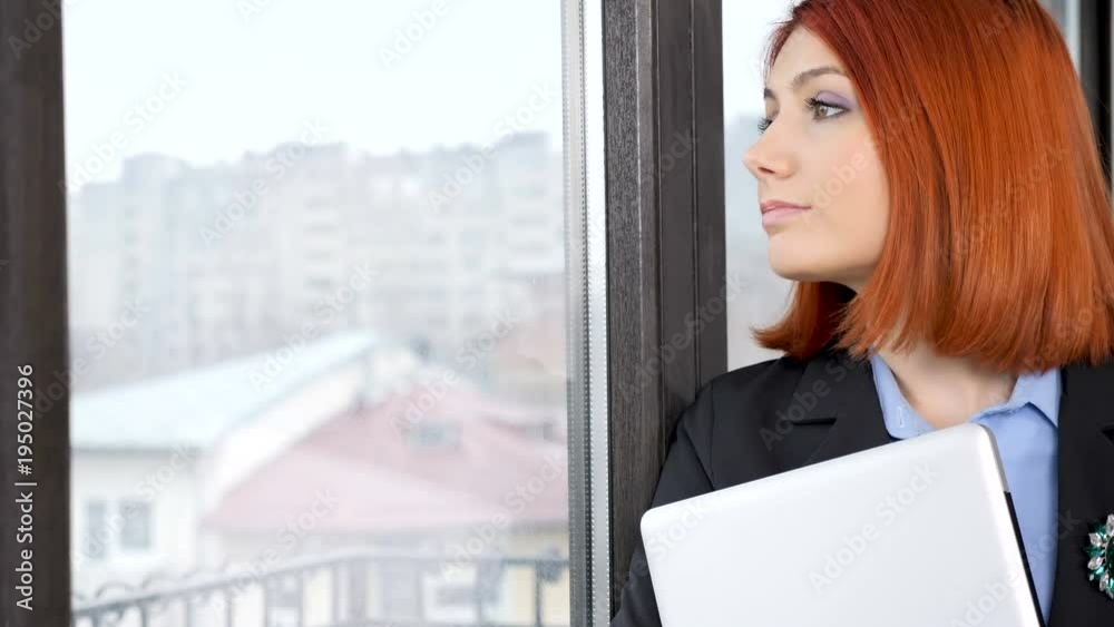 Sad businesswoman entering the frame with a laptop in hands and looking through the window Sad businesswoman entering the frame with a laptop in hands and looking through the window