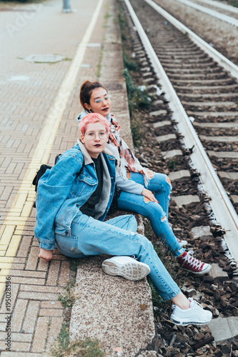 two young women sitting train station looking camera - best friends, bonding, interaction concept