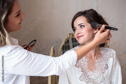 makeup artist preparing beautiful bride before the wedding in a morning