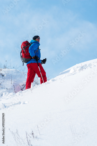 Smiling hiker, man in a sunglasses climbs the hill against the blue sky