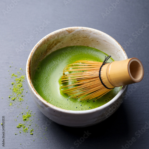 Matcha green tea cooking process in a bowl with bamboo whisk. Black slate background. Close up