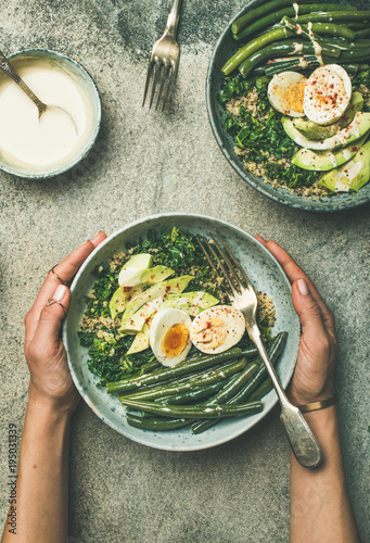 Healthy vegetarian breakfast bowls flat-lay. Quinoa, kale, green beans, avocado, egg and tahini dressing bowls over concrete background, top view. Energy boosting, clean eating, diet food concept