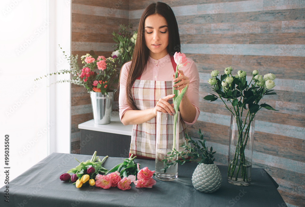 Female florist at work: pretty young dark-haired woman making fashion modern bouquet of different flowers. Women working with flowers in workshop