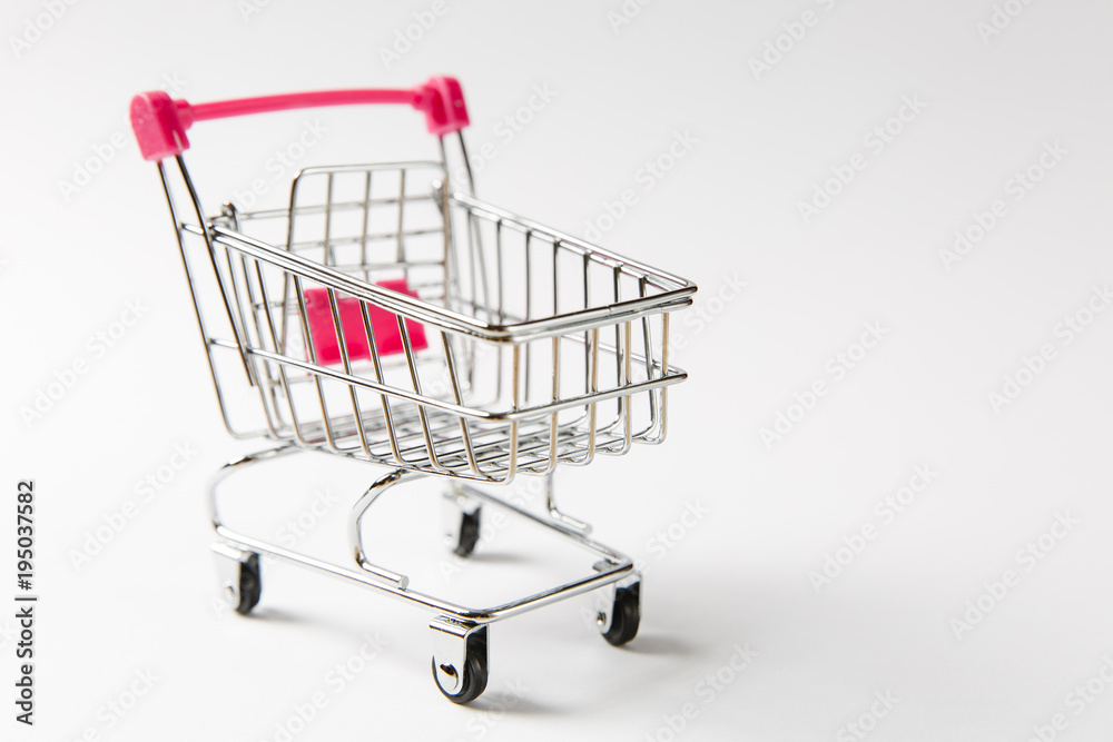 Close up of supermarket grocery push cart for shopping with black wheels and pink plastic elements on handle isolated on white background. Concept of shopping. Copy space for advertisement