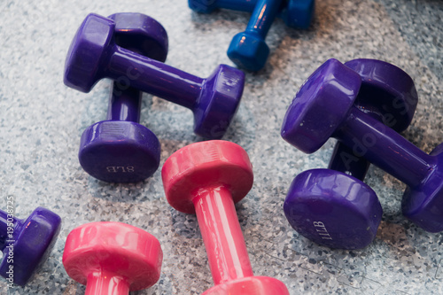 Purple and pink dumbbells lie on the gray floor at gym photo