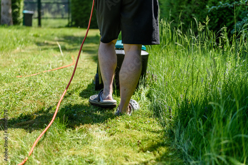 Man cutting grass with an electro lawnmower in his garden