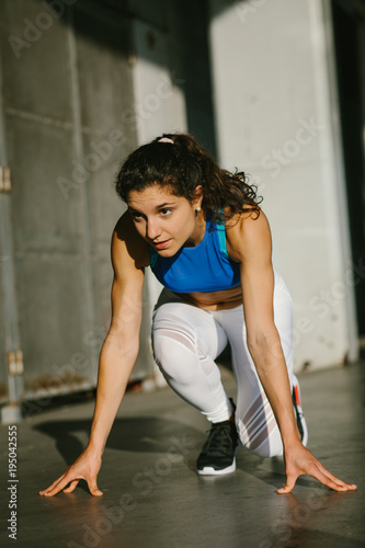 Focused female athlete getting ready for sprinting and running doing starting line pose. Fit young sporty woman training outside.