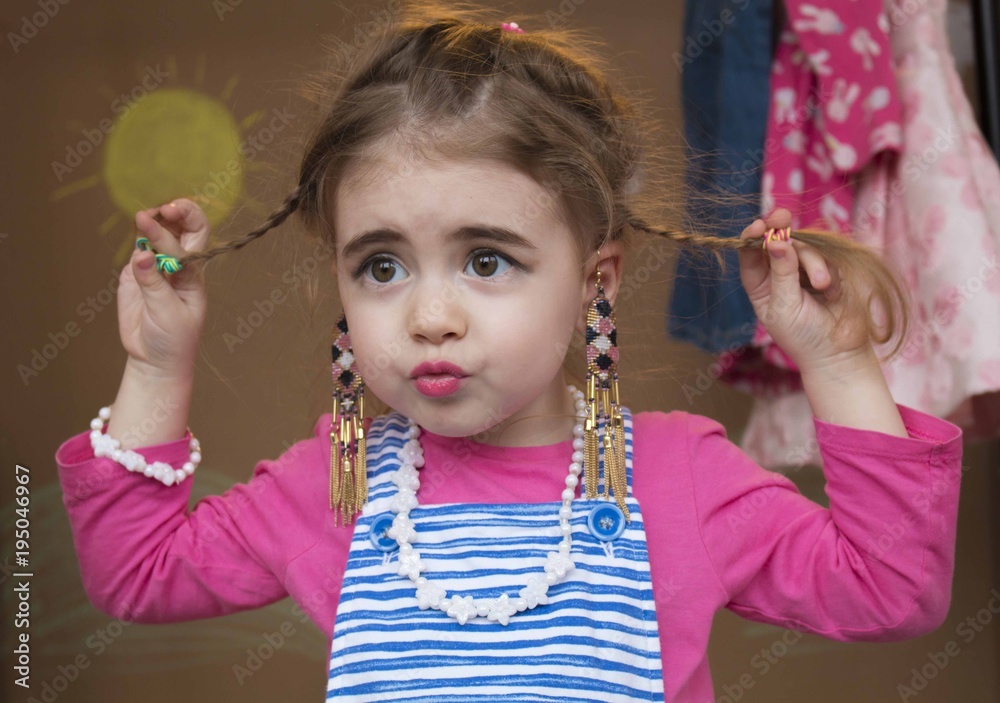 Clouse-up portrait emotional little girl with braided hair background of a clothes rack Clouse-up portrait emotional little girl with braided hair background of a clothes rack