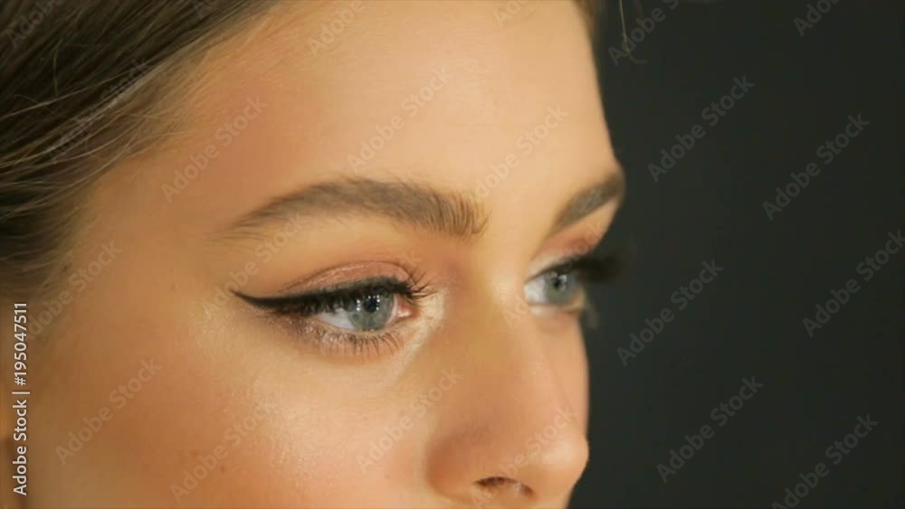 Beautiful model applying eyeliner closeup on eye, Close up, Make-up artist applying bright base color eyeshadow on model's eye and holding a shell with eyeshadow