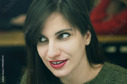 Beautiful girl behind the window. She is sitting in a nice cafe and looking through glass. City street is reflected in the window. It is evening time.
