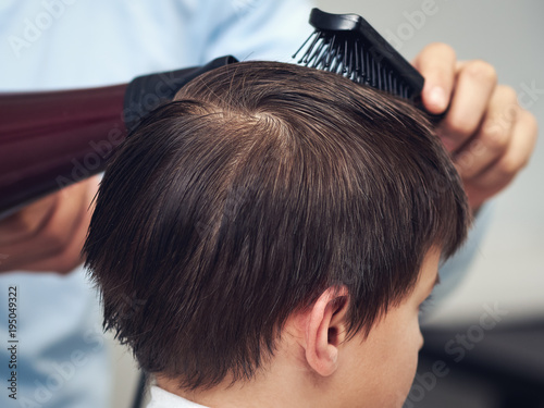 Boy getting haircut by hairdresser in barbershop.