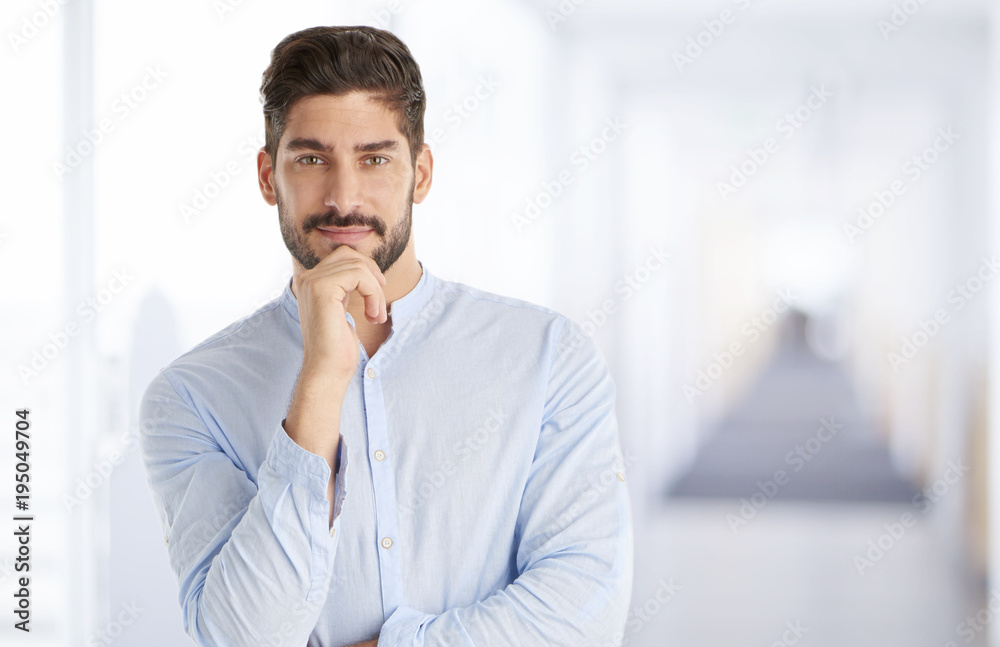 Confident young businessman portrait. Portrait of a casual young man standing at office, looking at camera and smiling. Confident young businessman portrait. Portrait of a casual young man standing at office, looking at camera and smiling.