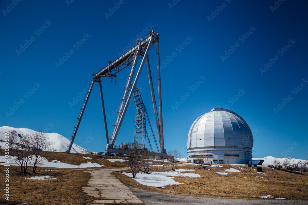 A special astrophysical observatory and a crane against the background of the blue sky and snowy peaks of the Caucasian mountains A special astrophysical observatory and a crane against the background of the blue sky and snowy peaks of the Caucasian mountains