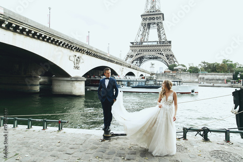 Luxury wedding couple poses before river Seine and the Eiffel Tower somewhere in Paris