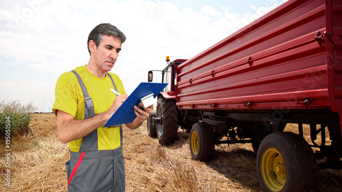 Foto Agronomist at Work During Wheat Harvest / Agronomist holding a clipboard and writing in front of a tractor on wheat field during harvesting