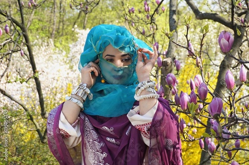Girl against of magnolia flowers in national Palestinian costume  with head covered. 