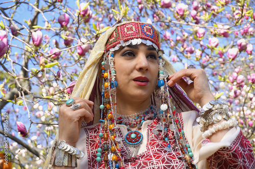 Girl against of magnolia flowers in national Palestinian costume, with head covered. 