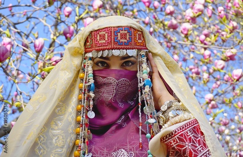 Girl against of magnolia flowers in national Palestinian costume, with head covered. 