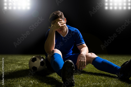 Footballer disappointed sitting on the grass field