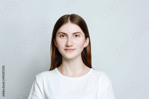 Model portrait without make-up in a white t-shirt on a white background. The girl poses in studio, smiling looking at camera. close up
