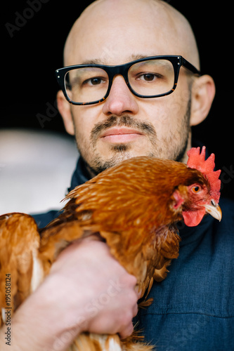 Strange unusual bald beardy man with serious senseless face in glasses standing in dark city tunnel. Oddball boy with chiken in hands. Adult male with lovely pet. Happy friends. Weird love. Birdman.