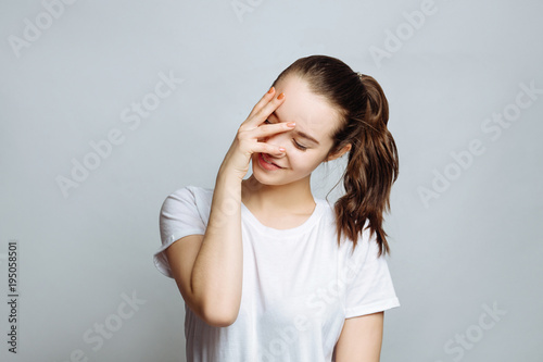 Portrait of a pretty woman brunette in a white t-shirt posing isolated on a white background. closing her eyes with hand, having happy expression, smiling broadly. waiting for pleasant surprise