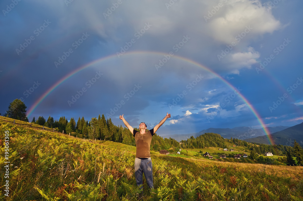 young guy, a tourist, raised his hands and thumbs up, rejoicing at the seen rainbow