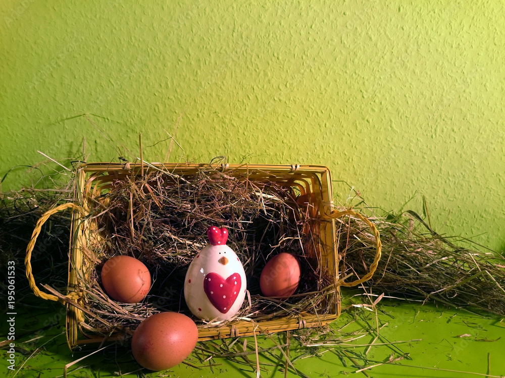 Osterkorb gefüllt mit Heu und braunen Eiern und einem Deko-Huhn mit grünem Hintergrund Osterkorb gefüllt mit Heu und braunen Eiern und einem Deko-Huhn mit grünem Hintergrund