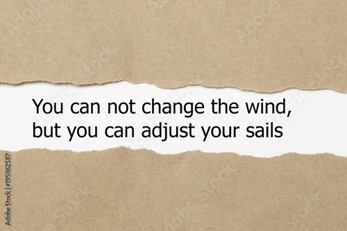 Motivational quote You can not change the wind but you can adjust your sails, appearing behind torn paper. photo