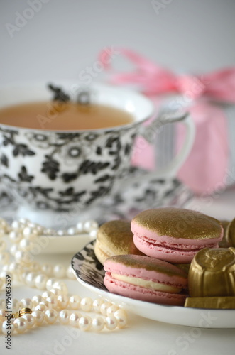 Gold and pink French macarons, chocolates with a cup of tea, pearls and an elegant pink gift-wrapped box. Luxurious gift. 