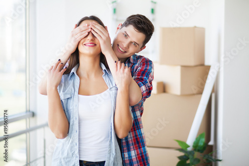 Couple showing keys to new home hugging, together unpacking cardboard boxes