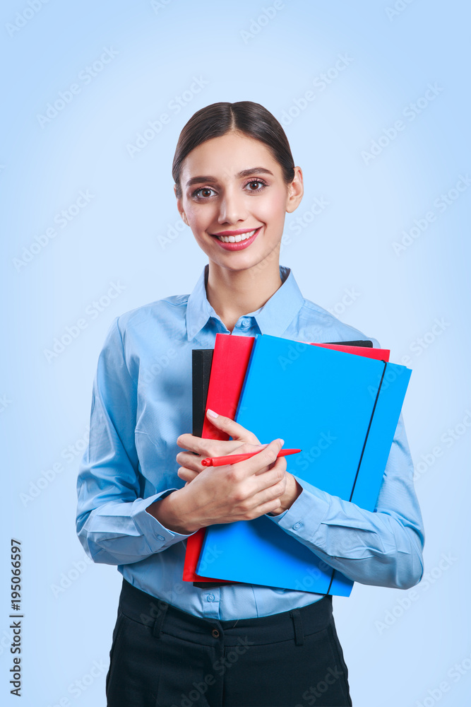 Businesswoman standing with folders and looking at camera on blue background Businesswoman standing with folders and looking at camera on blue background