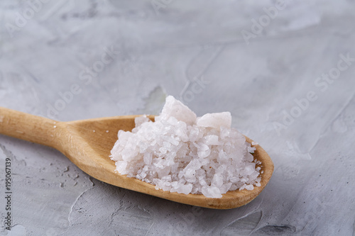 Crystal sea salt in a wooden spoon over light background, top view, close-up, selective focus