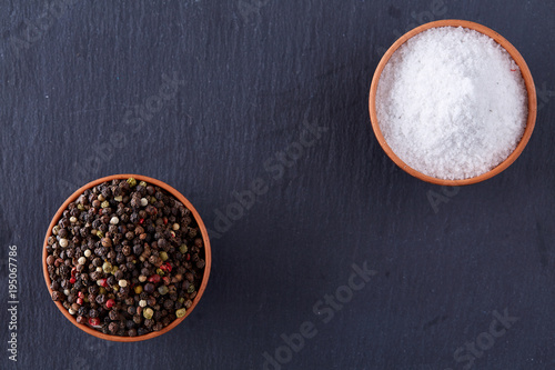 Conceptual composition of salt and pepper on spoons and bowls over dark background, top view, close-up
