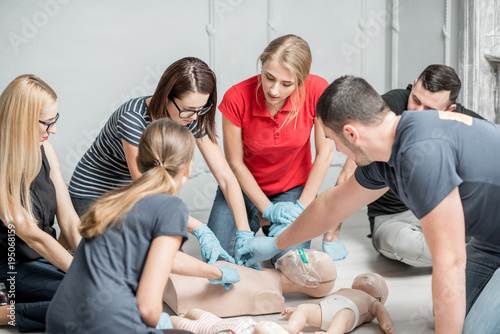 Group of people learning how to make first aid heart compressions with dummies during the training indoors photo