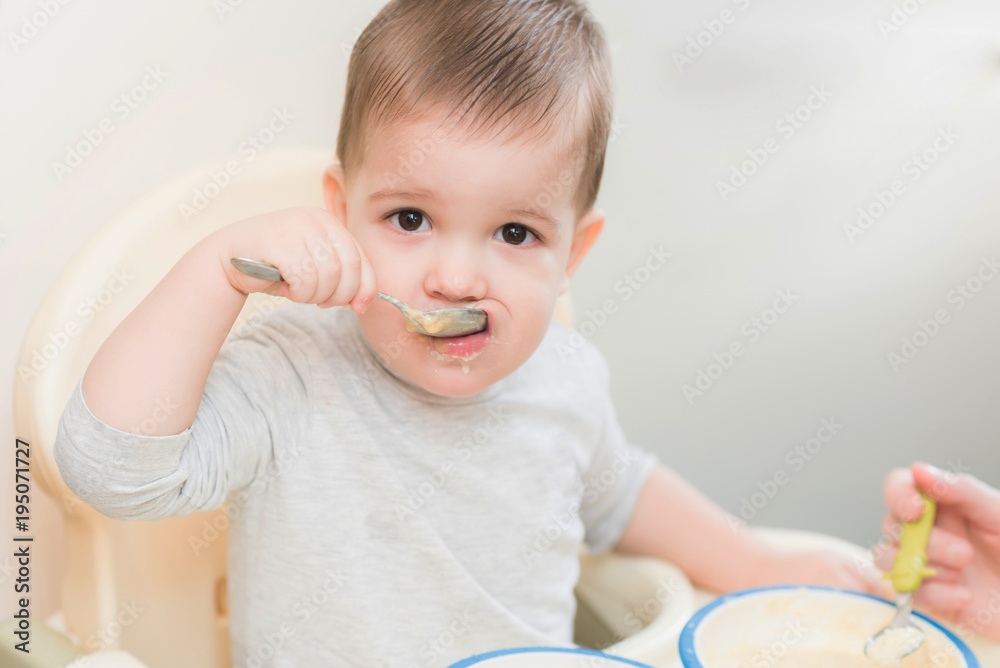 Fototapeta premium mom in the kitchen is feeding the baby milk porridge