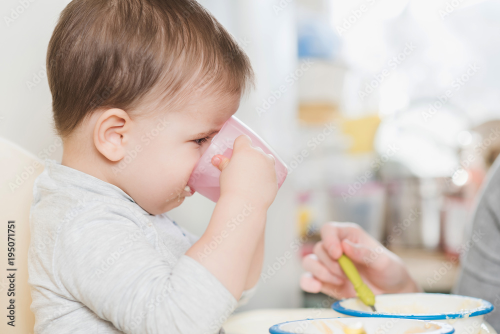 child in the kitchen drinking from a cup of water child in the kitchen drinking from a cup of water