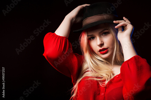 Adorable young woman in red blouse and brown hat posing at studio with shadow on her face © vpavlyuk