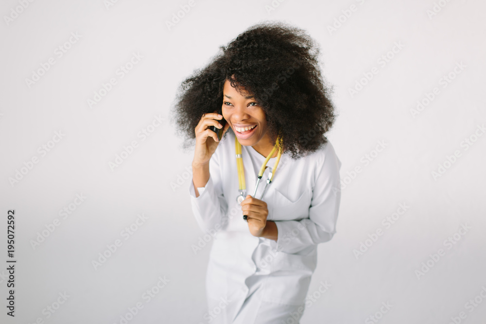 An African American female medical doctor with a stethoscope in hospital on white background and talking on the phone An African American female medical doctor with a stethoscope in hospital on white background and talking on the phone