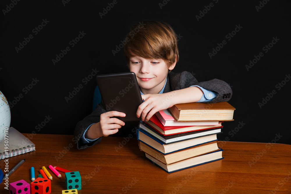 cute boy reading an e-book and sitting at a school desk . Back to school. cute boy reading an e-book and sitting at a school desk . Back to school.