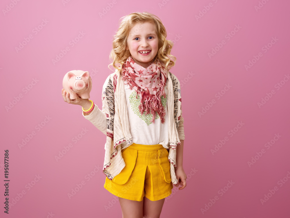 smiling modern child isolated on pink holding piggy bank
