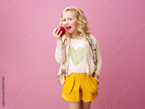 happy modern child isolated on pink eating an apple
