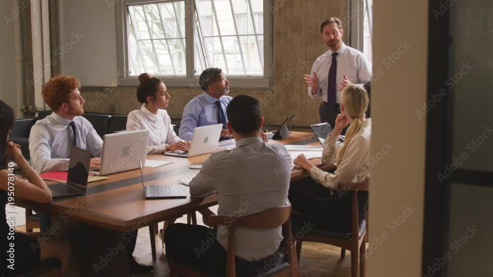 Middle aged businessman talks at meeting, seen from doorway Middle aged businessman talks at meeting, seen from doorway