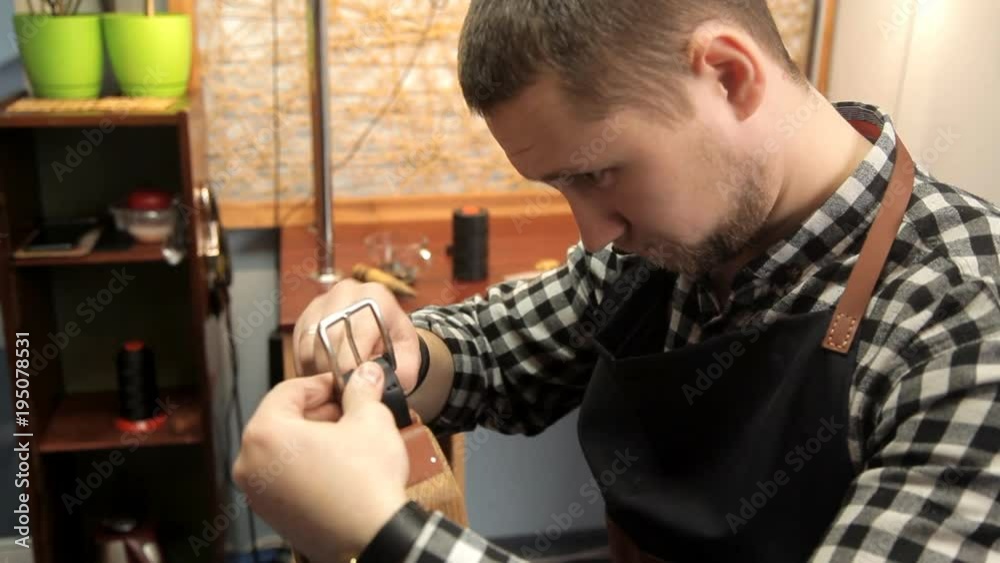 The master fastens the buckle on the leather belt, sews a needle. Procedure for the manufacture of leather belts The master fastens the buckle on the leather belt, sews a needle. Procedure for the manufacture of leather belts