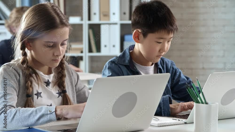 Two primary school students sitting in information technology class and typing something on laptop computer Two primary school students sitting in information technology class and typing something on laptop computer