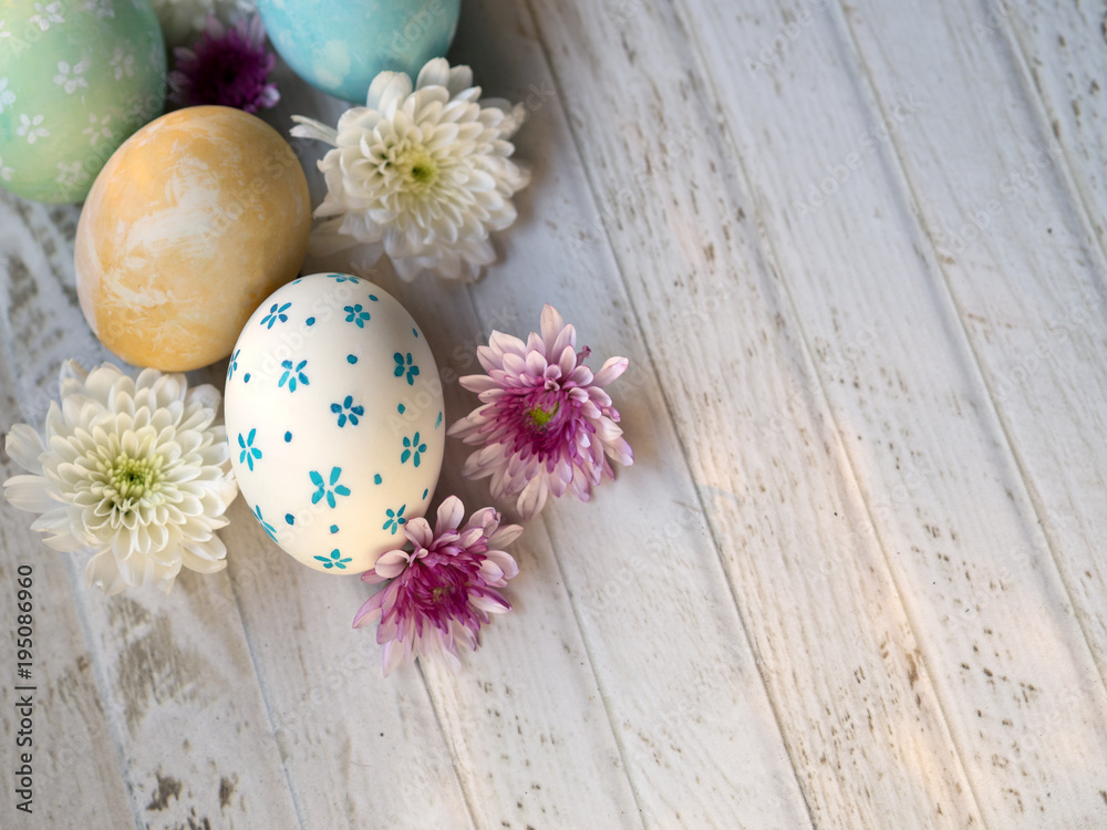 Cute and beautiful hand painting Easter eggs with white, yellow, blue and green color egg shells and pink and white color Spring flowers on white vintage wooden table, top view Cute and beautiful hand painting Easter eggs with white, yellow, blue and green color egg shells and pink and white color Spring flowers on white vintage wooden table, top view