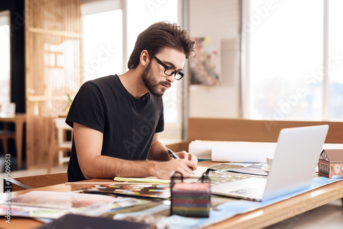 Freelancer bearded man taking notes at laptop sitting at desk. photo