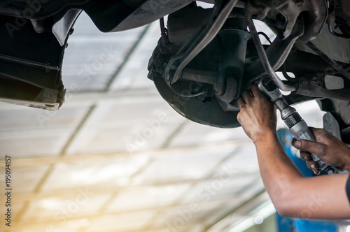 Auto mechanic asian checking bush-bolt under double wishbone suspension by hand with tools car lift 