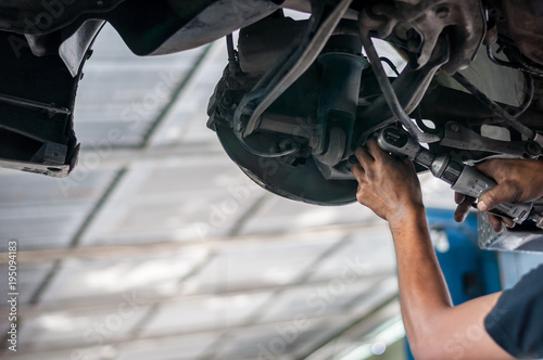 Auto mechanic asian checking bush-bolt under double wishbone suspension by hand with tools car lift 